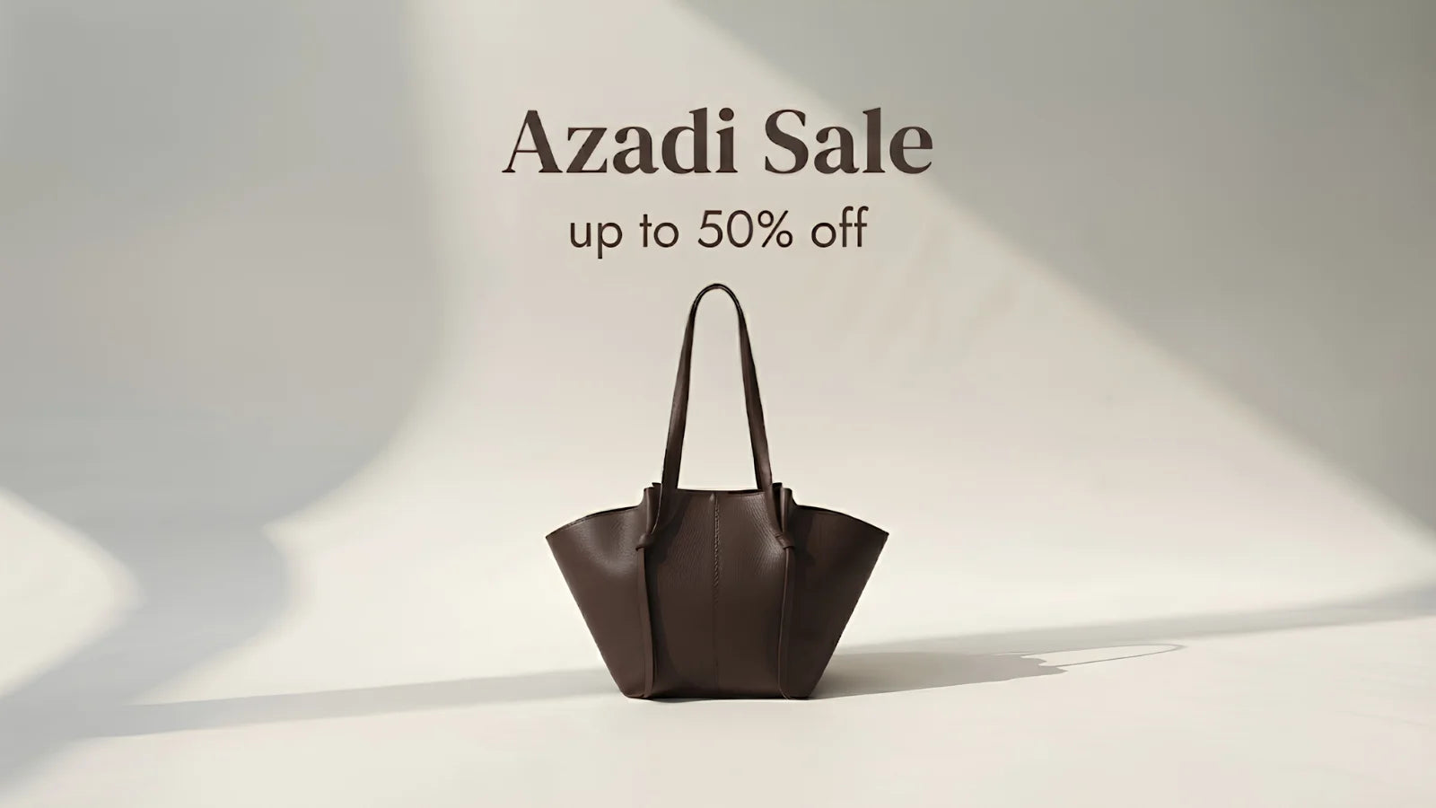 A dark brown leather tote bag stands on a light studio floor with text above reading 'Azadi Sale up to 50% off'.